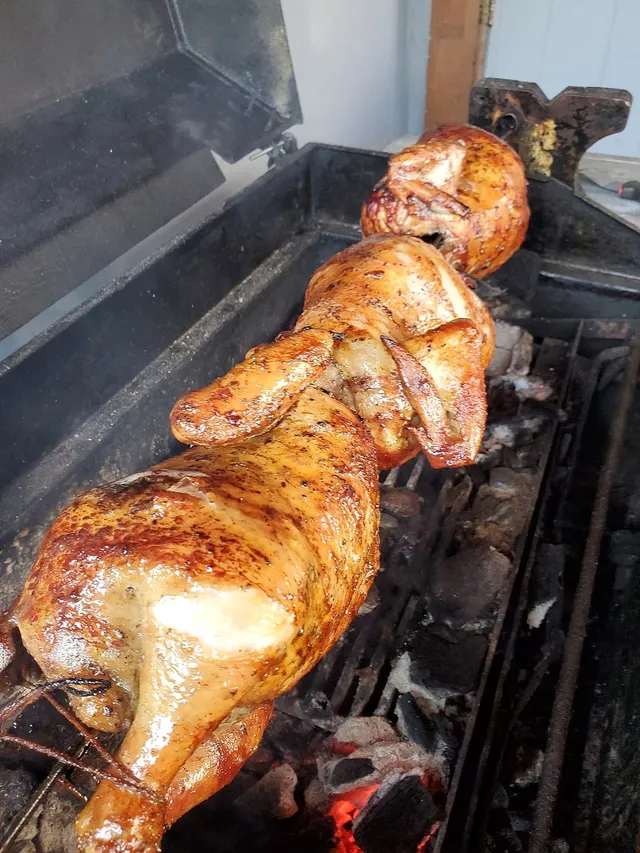 Whole chickens roasting on a spit over glowing charcoal